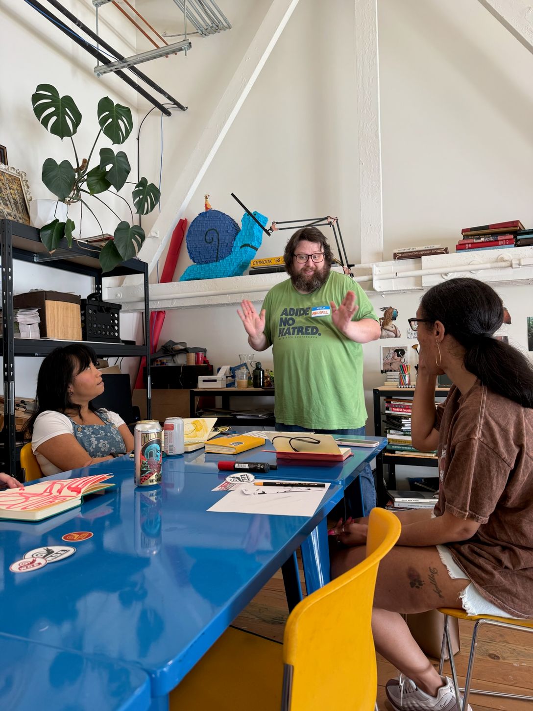 Michael, a bearded white man in a light green t-shirt leads a group of people in an art workshop.